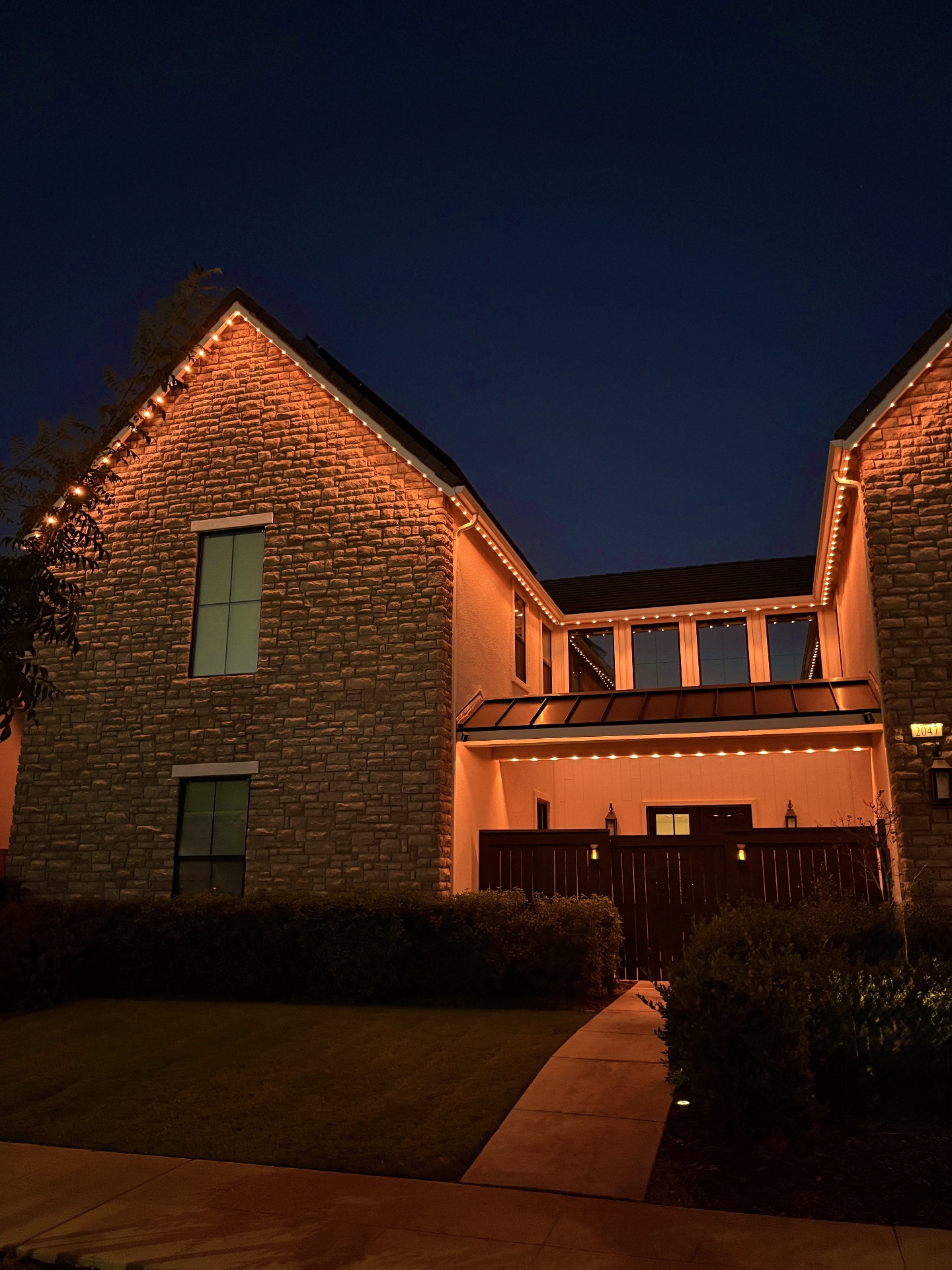 Stone-clad home glowing with warm amber bluEmber accent lighting along the gables and entryway