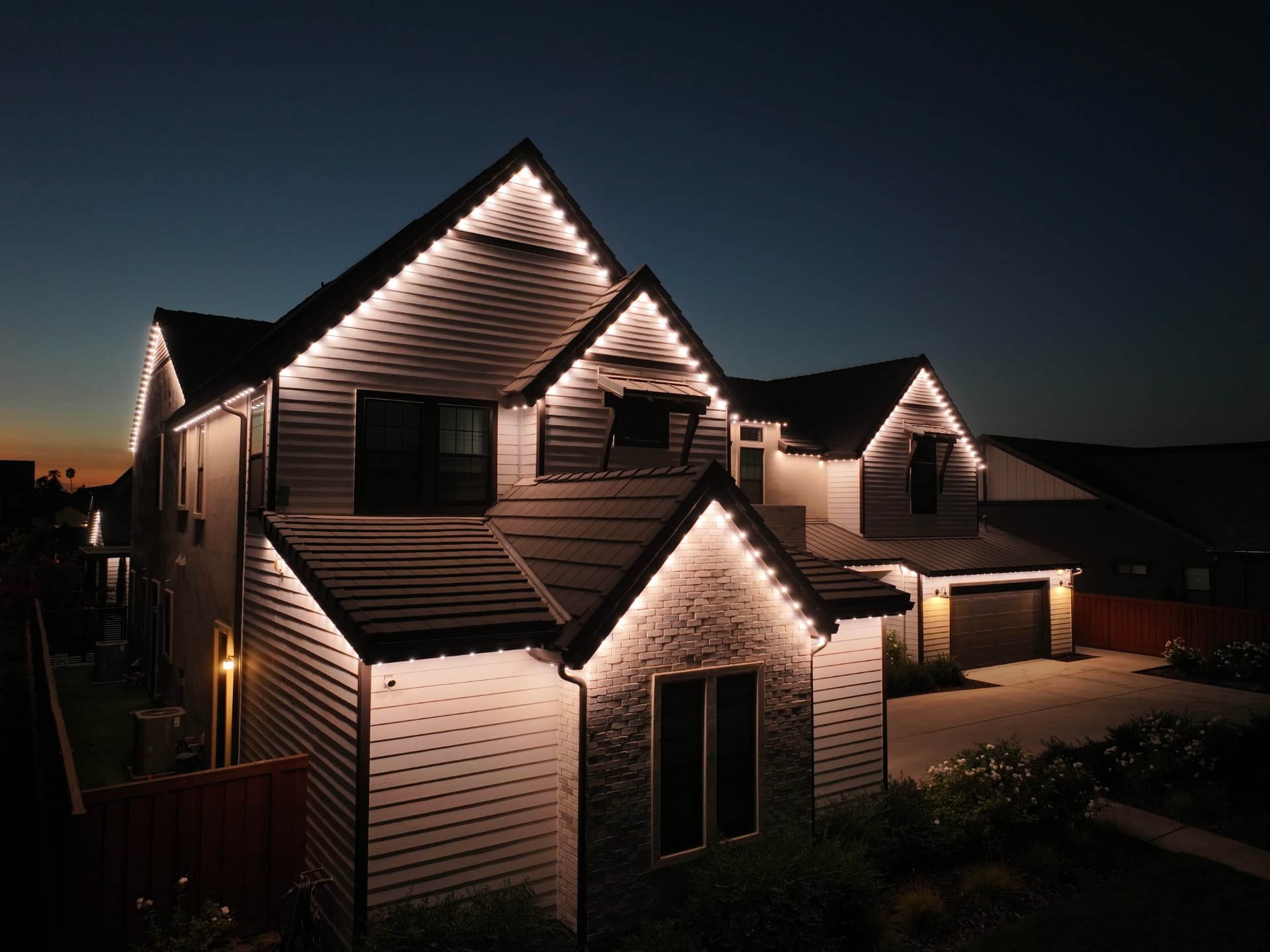 Two-story craftsman home glowing with warm-white bluEmber roofline lights at dusk