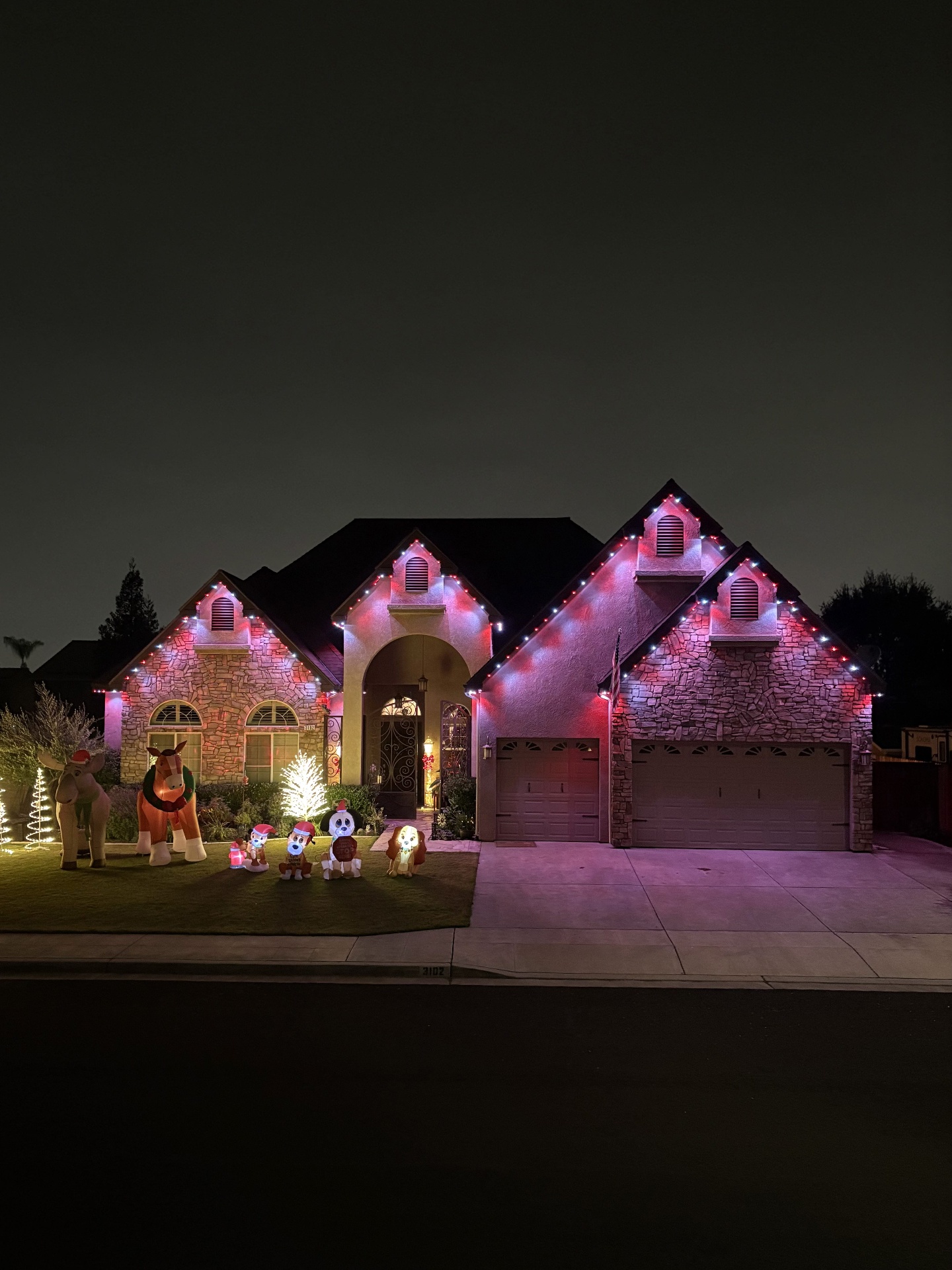 Suburban home in bluEmber red and white Christmas lights with festive yard inflatables