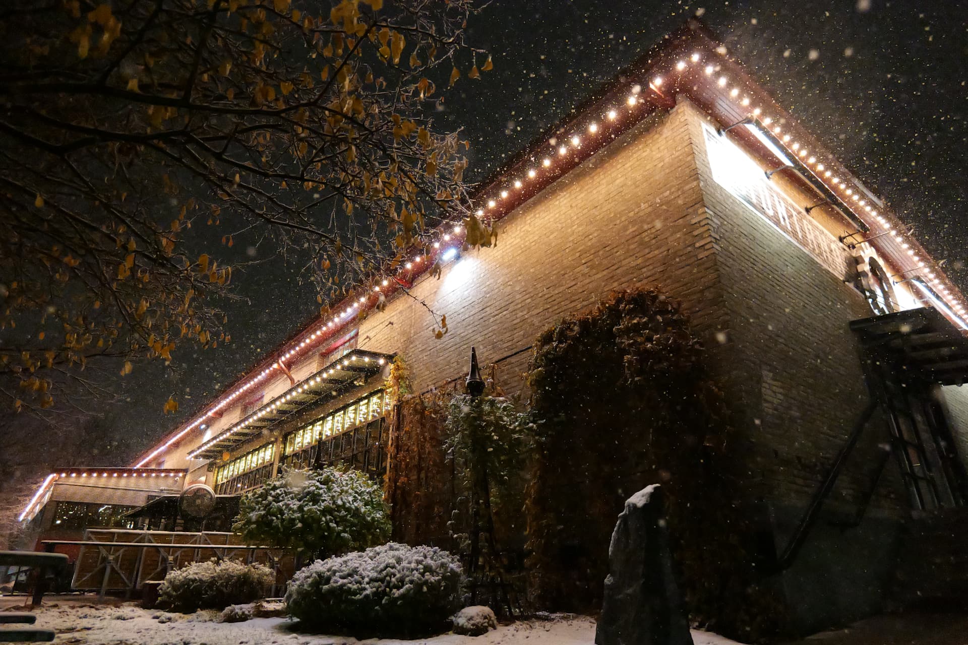 Snowy night view of a brick restaurant wrapped in warm-white bluEmber roofline lighting